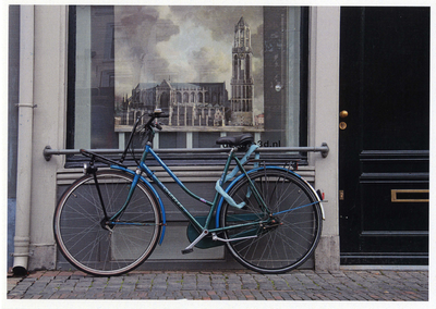 502268 Afbeelding van een blauwe damesfiets voor de etalage van het pand Oudegracht 18 te Utrecht, met achter het ...